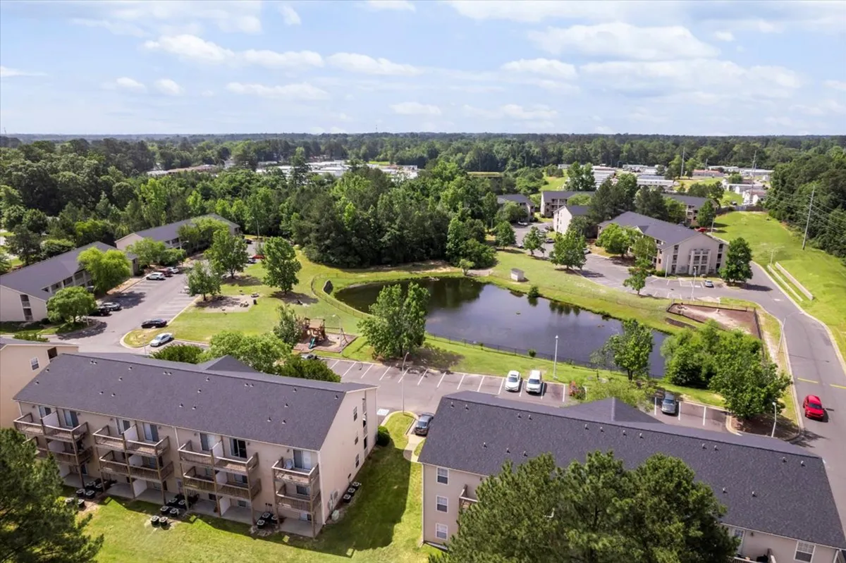 A serene scene featuring a tranquil pond, green open spaces, and apartment buildings in the background. Residents are seen walking, picnicking, or enjoying the natural setting, highlighting the community’s peaceful atmosphere and family-friendly amenities.
