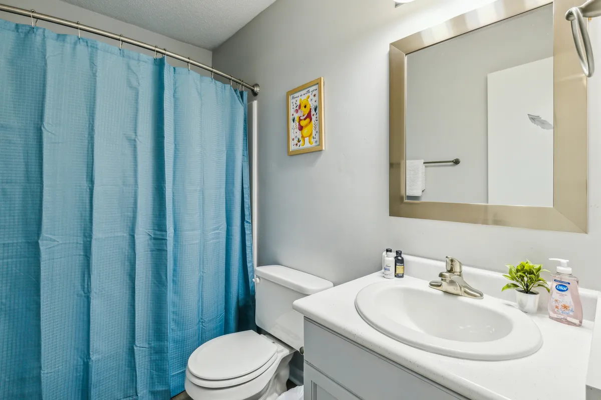 A bright, clean bathroom with a modern vanity sink, cheerful framed artwork, and a fresh shower curtain. The space is well-lit and organized—ready for both invigorating morning routines and relaxing evening rituals.