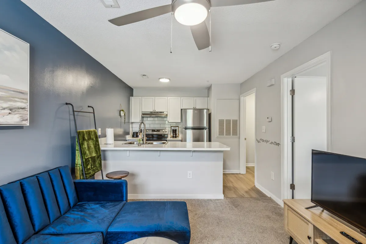 A modern, comfortable interior with a blue sectional sofa, a well-equipped kitchen featuring stainless steel appliances, and eye-catching artwork. The space feels bright and inviting, perfect for both relaxing and preparing meals at home.