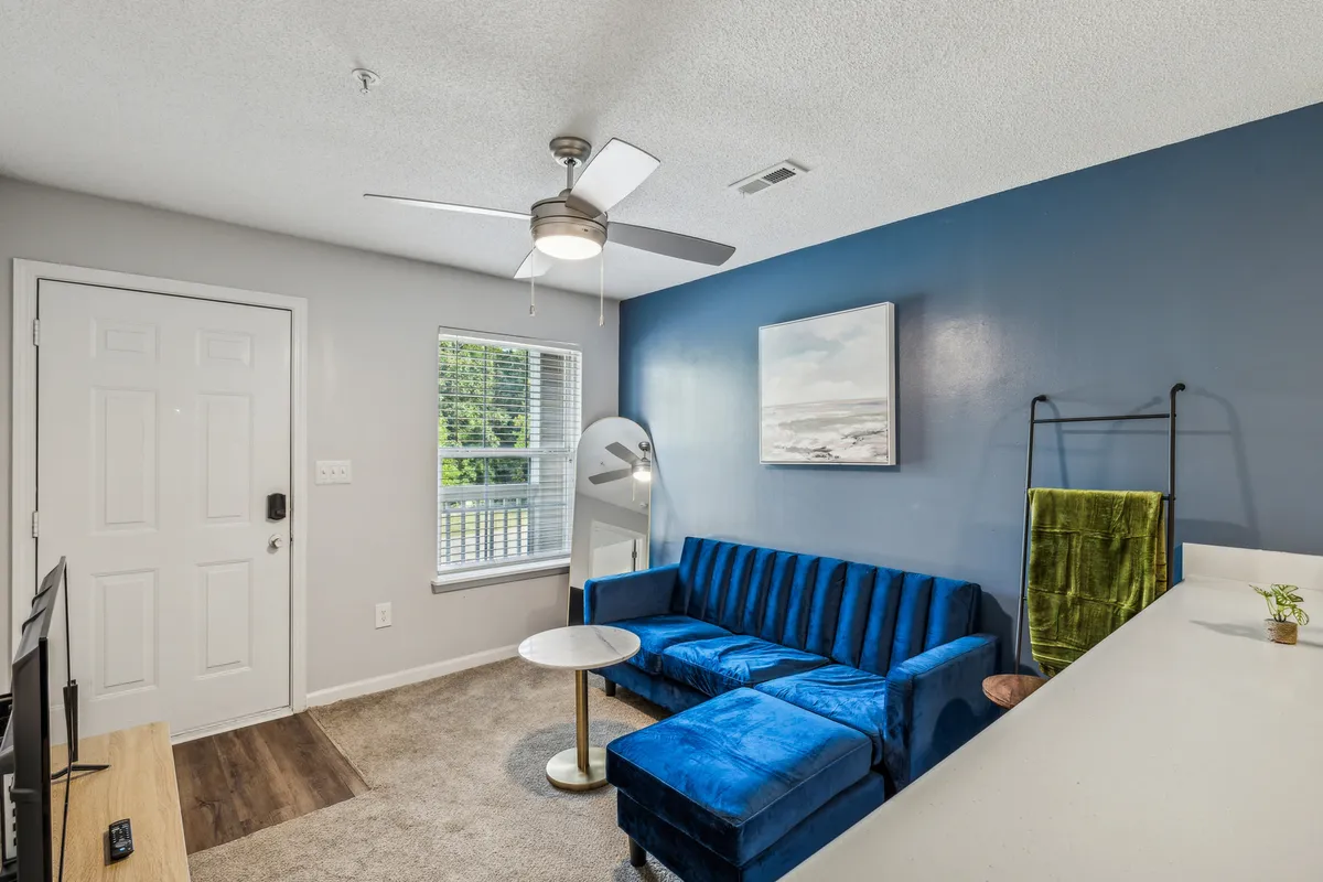 This image features a cozy blue couch adorned with throw pillows, a round coffee table at the center, and tasteful artwork on the wall. The living area is bright, modern, and inviting, designed for relaxation and socializing.