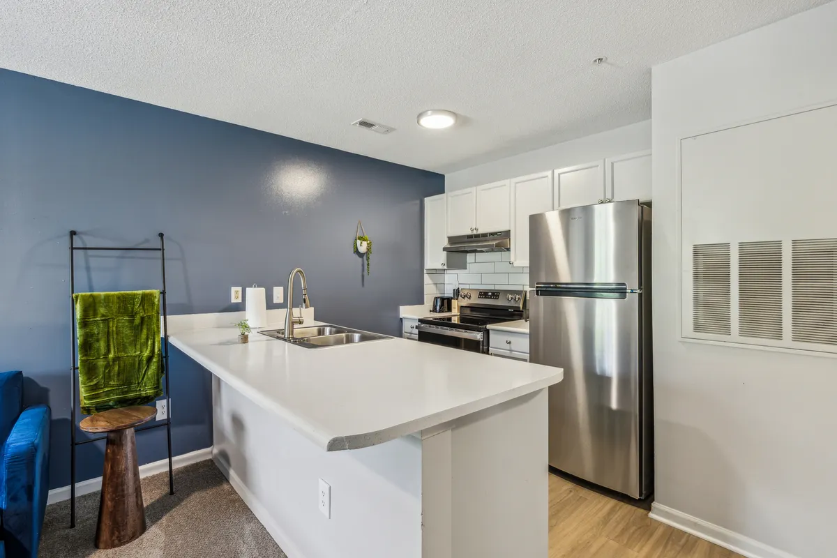 A contemporary kitchen with a central island, stainless steel appliances, a bold blue accent wall, and a green towel for a pop of color. The setting is inviting and functional, with ample counter space and seating, perfect for cooking, entertaining, or casual dining.