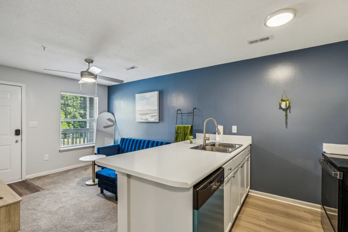 A modern living space with a blue couch, kitchen island, and wall art, providing a glimpse of both lounging and dining areas. The setting is airy, comfortable, and designed for social or solitary relaxation.